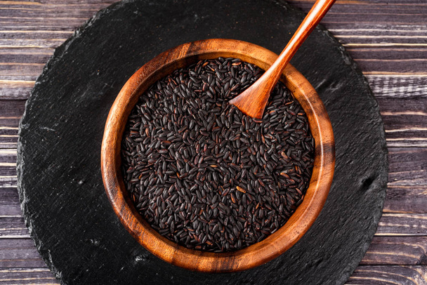 Isolated handful of raw black (nero) rice in the wood bowl on bl - Photo, Image