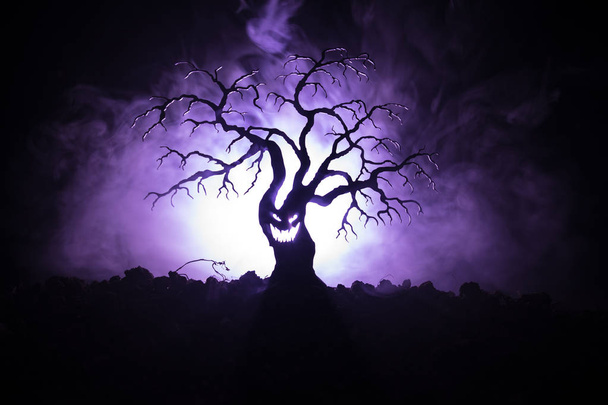 Silhouette of scary Halloween tree with horror face on dark foggy toned background with moon on back side. Scary horror tree with zombie and demon faces. - Photo, Image