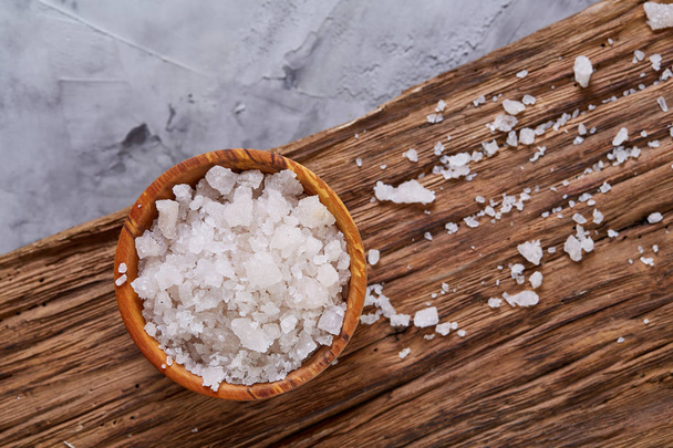 Large white sea salt in a natural wooden bowl on white background, top view, close-up, selective focus - 写真・画像