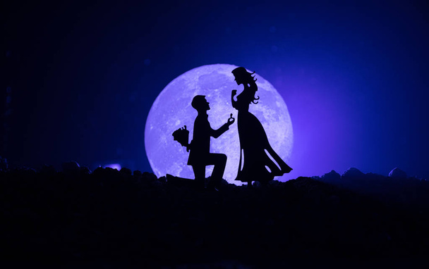 Geweldige scène van de liefde. Silhouetten van man vrouw of silhouetten van paar tegen grote maan bij achtergrond worden voorstel aangebracht - Foto, afbeelding