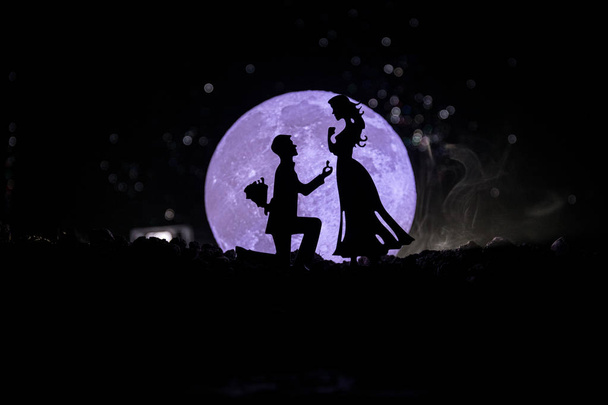 Geweldige scène van de liefde. Silhouetten van man vrouw of silhouetten van paar tegen grote maan bij achtergrond worden voorstel aangebracht - Foto, afbeelding