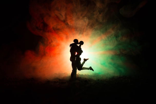 Love Valentine`s Day concept.Sillhouette of sweet young couple in love standing in the field and hugging on dark toned foggy background. Decoration with doll figures on table shot. - Фото, зображення