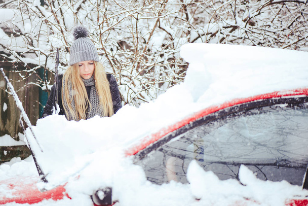 Χειμώνα πορτρέτο μιας νεαρής γυναίκας που τον καθαρισμό χιόνι από ένα αυτοκίνητο. Ξανθιά ομορφιά κορίτσι μοντέλο γελάει και χαρωπά καθαρίζει το χιόνι. Όμορφη νεαρή γυναίκα σε εξωτερικούς χώρους - Φωτογραφία, εικόνα