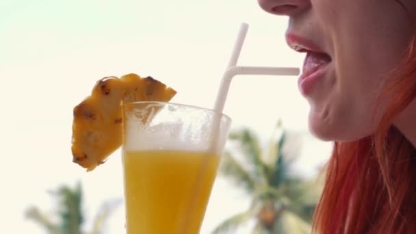 young woman drinks a strawberry pineapple cocktail from a glass - Video