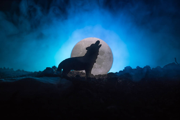 Silhouette eines heulenden Wolfes vor dunkel getöntem Nebelhintergrund und Vollmond oder Wolf in Silhouette, der zum Vollmond heult. Halloween-Horror-Konzept. - Foto, Bild
