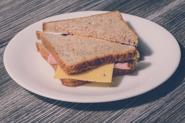白い丸皿においしいチーズ ソーセージのサンドイッチ。木製の背景、水平ビュー、ヴィンテージ効果 - 写真・画像