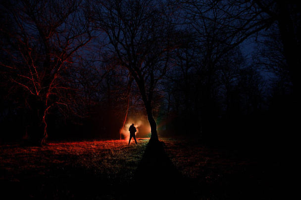 seltsames Licht in einem dunklen Wald in der Nacht. Silhouette einer Person, die im dunklen Wald mit Licht steht. dunkle Nacht im Wald zur Zeit des Nebels. surreale nächtliche Waldszene. Horror-Halloween-Konzept. - Foto, Bild