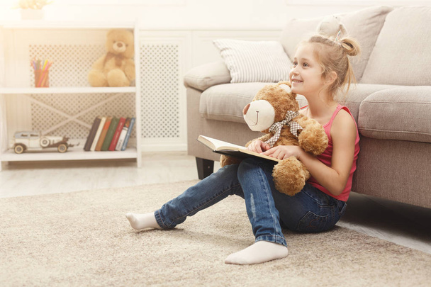 Boldog kis női gyermek és ő könyvével a padlón otthon mackó - Fotó, kép