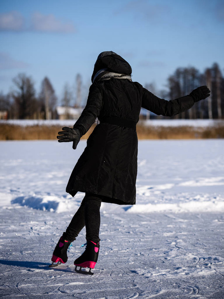 νεαρή γυναίκα στο μαύρο παλτό πατινάζ στην παγωμένη λίμνη στο χιόνι, le - Φωτογραφία, εικόνα