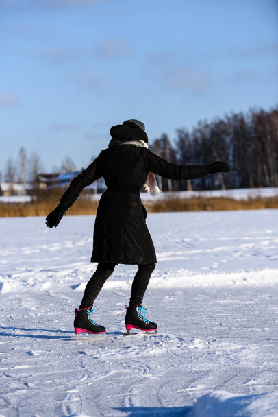 young woman in black coat skating on the frozen lake in snow, le - Photo, Image