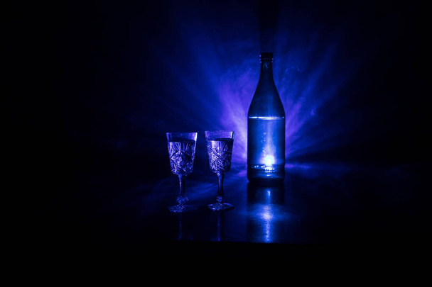 Δύο ποτήρια βότκα με μπουκάλι σε σκοτεινό, ομιχλώδη club στυλ φόντου με λαμπερό παραδεισένιους φώτα (Laser, Stobe). Λέσχη ποτά θέμα διακόσμησης. Κενός χώρος - Φωτογραφία, εικόνα