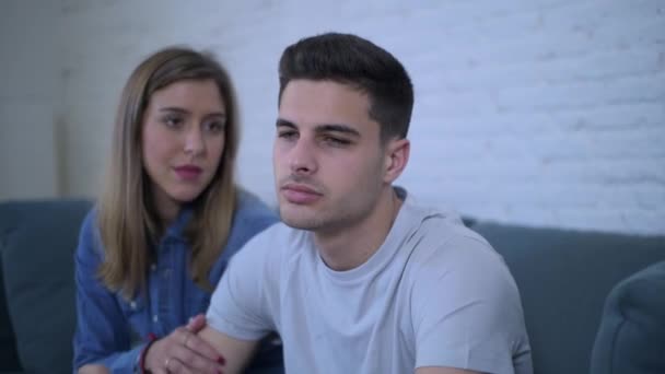 Lateral pan shot of young attractive couple with boyfriend sad frustrated and depressed at home couch and girlfriend comforting and consoling him in relationship support love emotions and lifestyle concept - Materiał filmowy, wideo