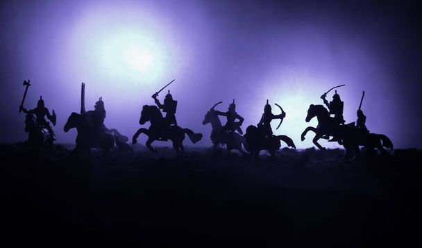 Medieval battle scene with cavalry and infantry. Silhouettes of figures as separate objects, fight between warriors on dark toned foggy background. Night scene. - Photo, Image