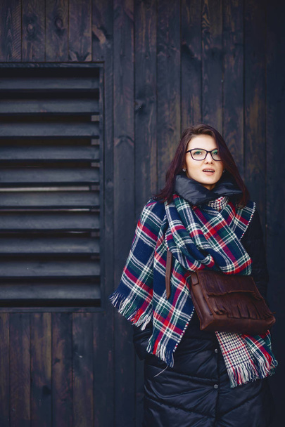 mooi meisje in brillen en een sjaal tegen een houten muur - Foto, afbeelding