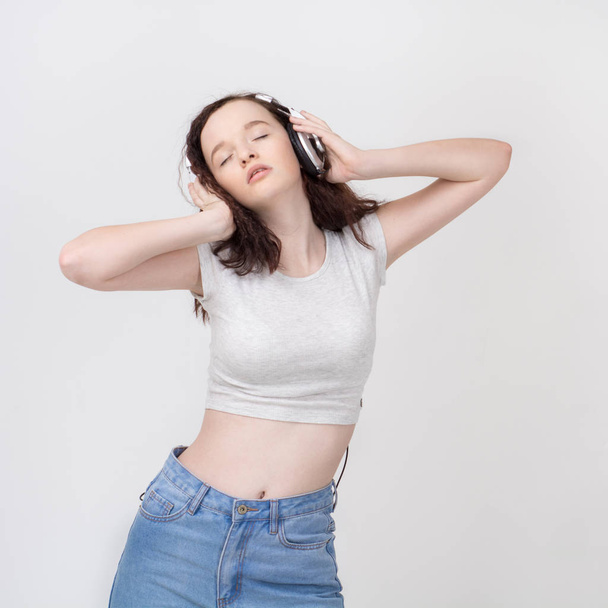 Portrait of a young beautiful girl with curly hair eyes closed with headphones listening to music on white background - Φωτογραφία, εικόνα