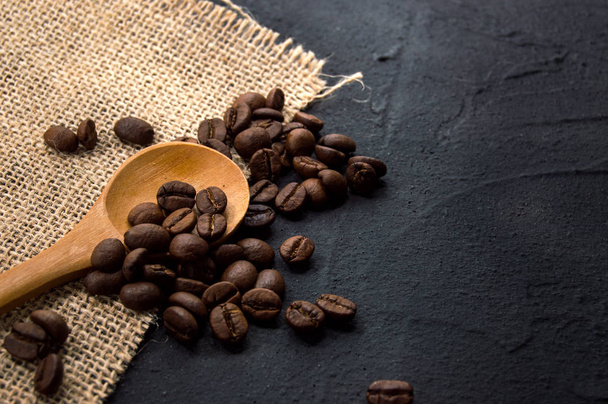 Coffee beans in burlap fabric and wooden spoon on dark cement background - Photo, Image