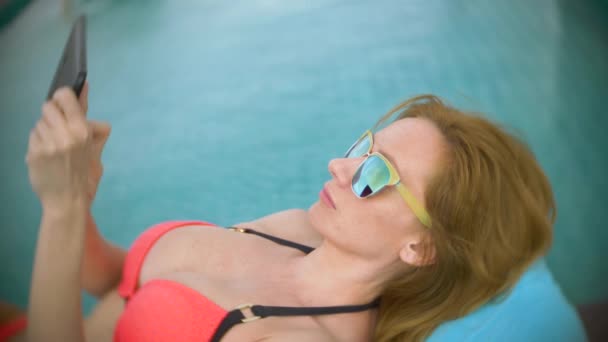 Nainen vaaleanpunaisissa bikineissä katon uima-altaalla, tyttö aurinkotuolissa ja käyttää puhelinta. 4k, hidasta.
 - Materiaali, video