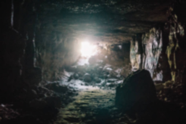Flucht aus der Dunkelheit Konzept. verschwommenes und defokussiertes Foto eines dunklen unterirdischen Kalksteinhöhlentunnels oder -korridors mit Licht und Ausgang am Ende - Foto, Bild