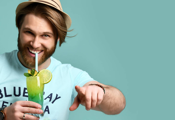 Молодой человек в шляпе держит коктейль Маргарита сок счастливый улыбаясь указывая пальцем в камеру
 - Фото, изображение