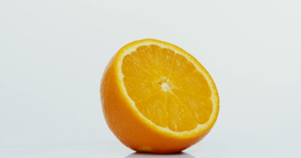 Close up of the half of the orange rolling in front of the camera on the white background. Macro - Кадры, видео