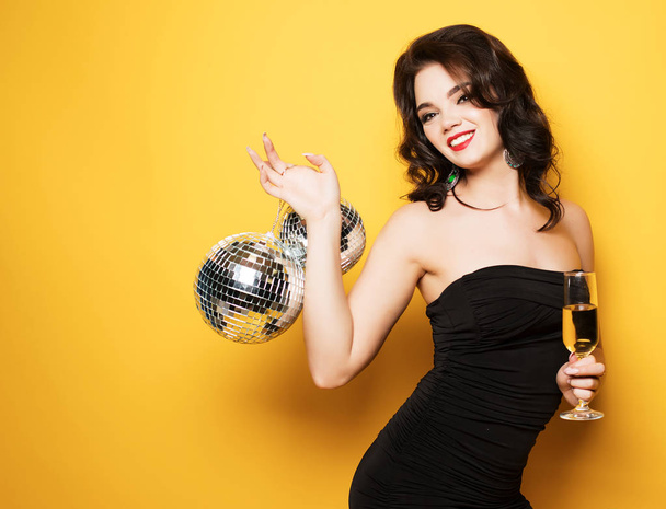 sexy woman with a glass of white wine and disco ball over yellow background - Fotoğraf, Görsel
