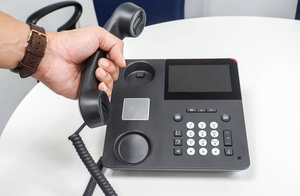primer plano hombre de negocios que usa el teléfono del asimiento del reloj del teléfono IP en la mesa con la mano izquierda para llamar
 - Foto, imagen