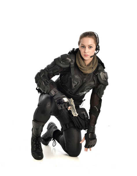 Pełna długość Portret żołnierz Kobieta w czarnej zbroi taktyczne, siedzącej pozie trzyma broń, na białym tle na tle białego studia. - Zdjęcie, obraz