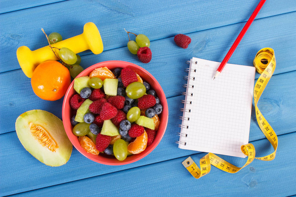 Fruit salad, tape measure with dumbbells and notepad for writing notes, healthy lifestyle and nutrition concept - Фото, зображення