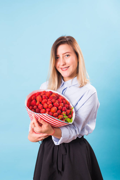 Young woman holding bouquet of strawberries on blue background. - Valokuva, kuva
