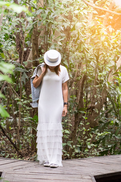 Onnellinen nainen yllään valkoinen maxi mekko denim takki julkisessa puistossa. Käsite onnellinen elämä luonnon kanssa
. - Valokuva, kuva