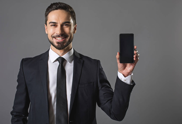 Smiling handsome businessman showing modern smartphone - Foto, Bild
