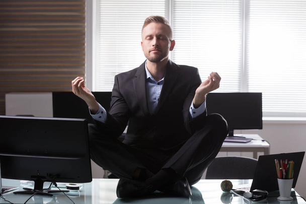 Young Businessman Sitting On Desk Meditating In Office - Fotoğraf, Görsel