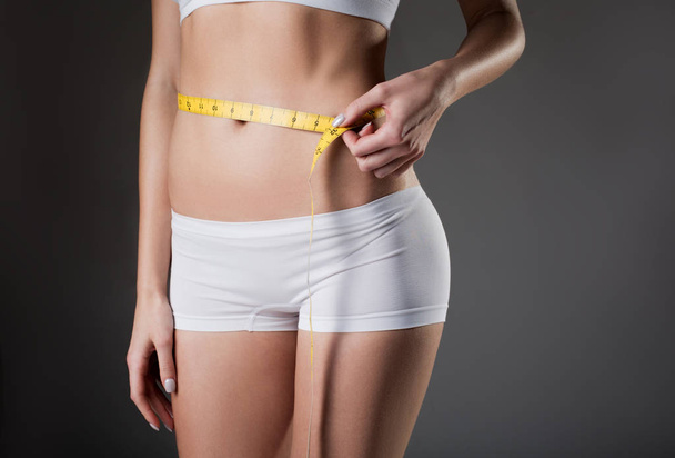 Slim young woman taking measurements of waistline - 写真・画像