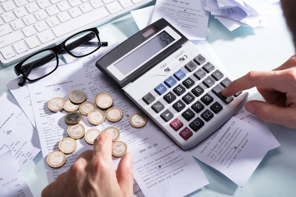 Businessperson's Hand Calculating Receipt With Coins And Eyeglasses On Desk - Foto, immagini
