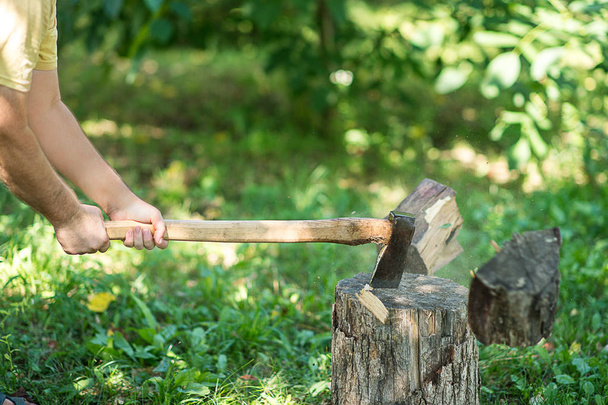 Ο άνθρωπος κόβει ξύλα με το τσεκούρι για ένα πράσινο γρασίδι.  - Φωτογραφία, εικόνα