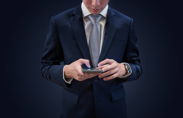 Businessman in dark blue suit using mobile smart phone, on blue background - Фото, изображение