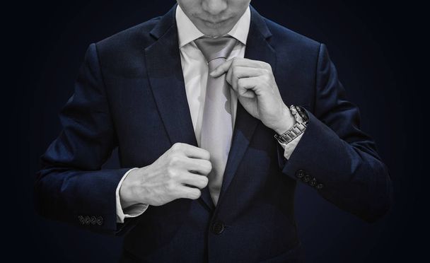 青の背景にグレーのネクタイを結ぶダークブルーのスーツのビジネスマン - 写真・画像