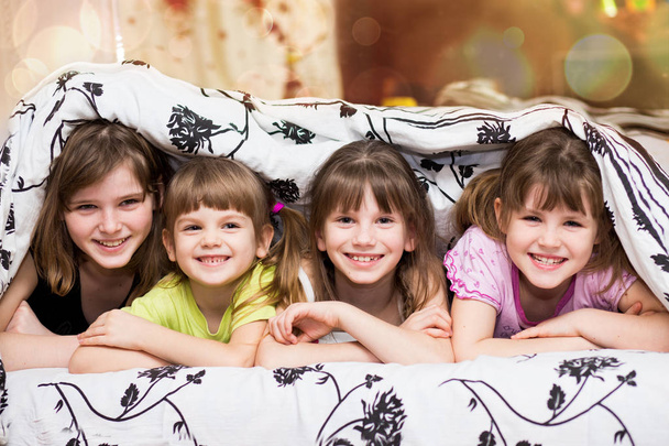 Смешные сестрички прячутся под одеялом. Милые девочки веселятся на кровати. Концепция детского сна, ухода или детства
 - Фото, изображение