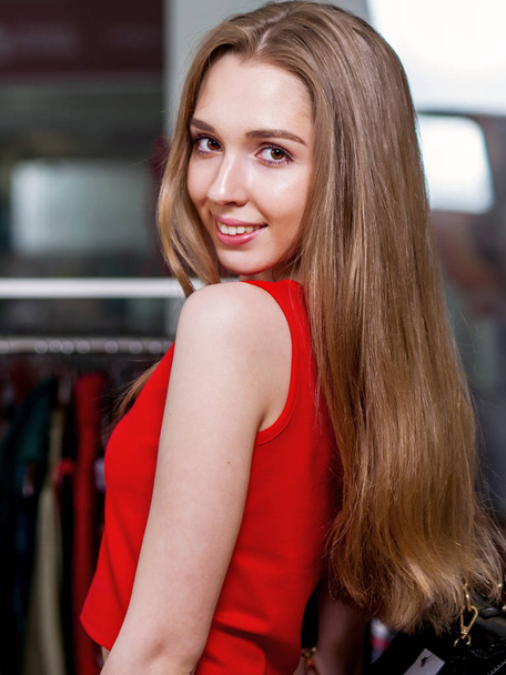 Portrait of female model wearing red dress with long fair hair looking back in shopping mall - Valokuva, kuva