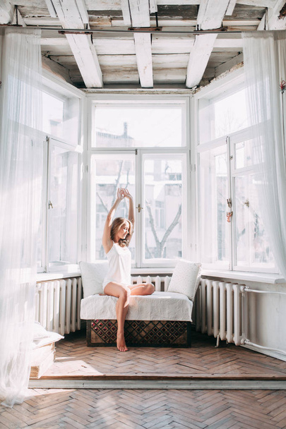 Portrait of pretty young girl on bed in modern Sunny apartment in the morning. Sipping and smiling, drinking coffee and lying on the floor - Photo, image