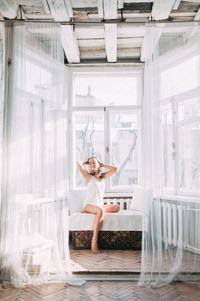 Portrait of pretty young girl on bed in modern Sunny apartment in the morning. Sipping and smiling, drinking coffee and lying on the floor - Valokuva, kuva