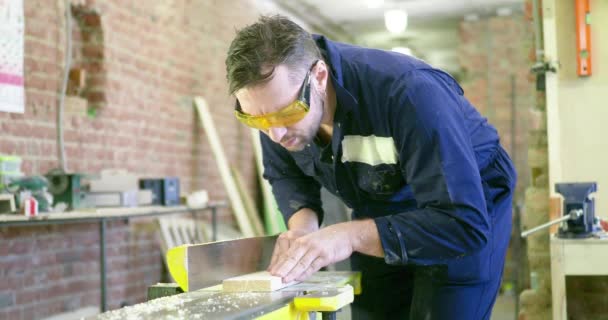 Un homme dans un atelier de menuiserie porte des lunettes de protection. Il traite le tableau sur une machine électrique. Vidéo 4K
 - Séquence, vidéo