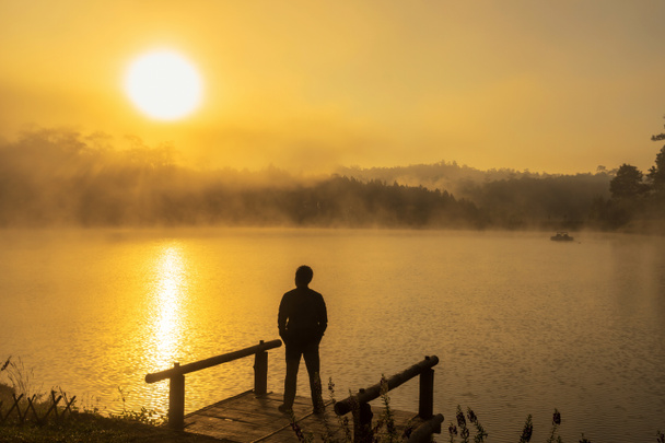 孤独の概念と劇的な日の出時に屋形船川湖に立っているシルエット落ち込んでいる人 - 写真・画像