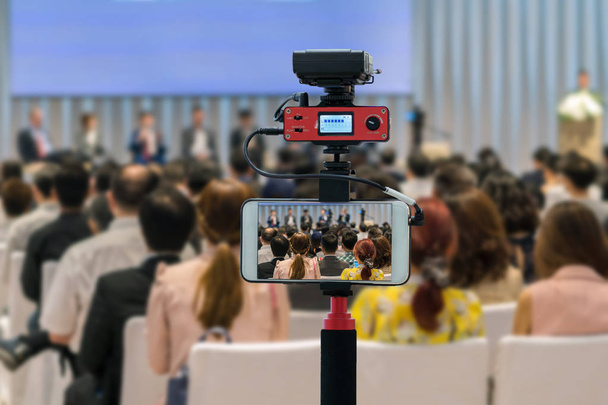 Έξυπνο κινητό τηλέφωνο closeup ανάληψη ηχεία Live στη σκηνή με την πίσω όψη του κοινού στην αίθουσα ή σεμινάριο διάσκεψη, τεχνολογία live streaming και εκπομπή έννοια - Φωτογραφία, εικόνα