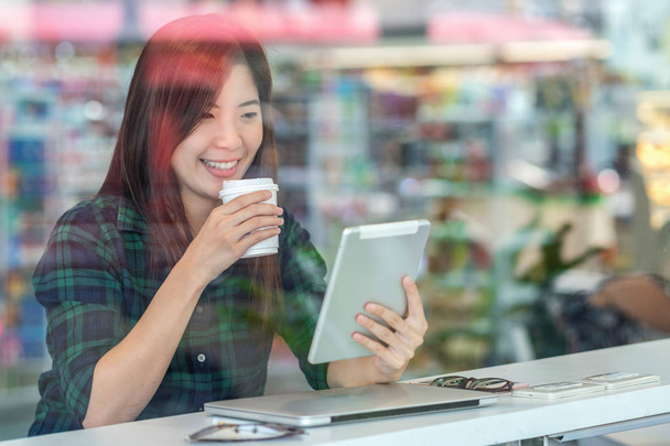Portret van Aziatische zakenvrouw in casual pak drinken en met behulp van technologie laptop voor het werken in geluk actie bij balie naast glas in moderne kantoor. Business en lifestyle concept - Foto, afbeelding