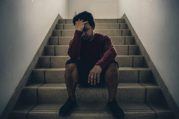 Καταθλιπτική άνθρωπος κάθεται το κεφάλι στα χέρια στην σκάλα σε πυρκαγιά διαφυγής ή κτίριο σκάλες με περιβάλλον χαμηλού φωτός, δραματική σκηνή έννοια - Φωτογραφία, εικόνα