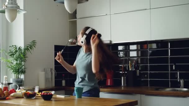 Cheerful young funny woman dancing and singing with ladle while having leisure time in the kitchen at home - Záběry, video
