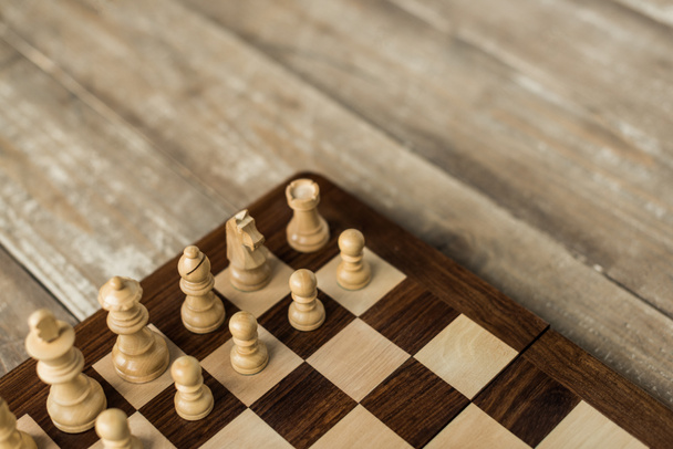 Cropped view of chess board with white chess pieces on rustic wooden surface - Foto, afbeelding