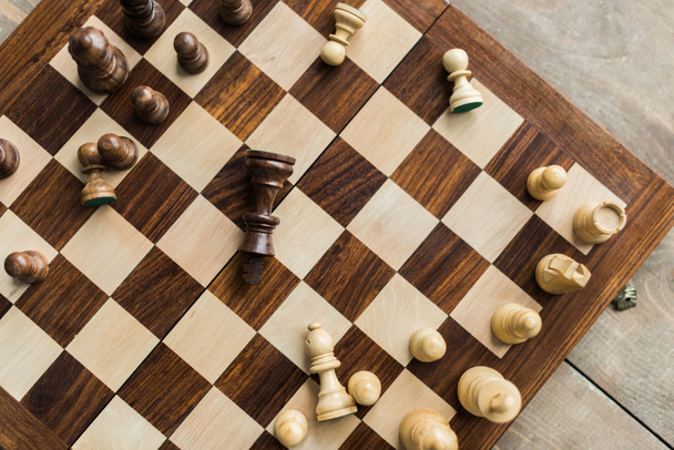 Tablero de ajedrez con figuras de ajedrez dispersas sobre superficie de madera
 - Foto, Imagen