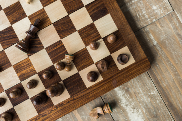 Schaakbord met verspreide zwarte schaakstukken op rusitc houten oppervlak (bovenaanzicht) - Foto, afbeelding